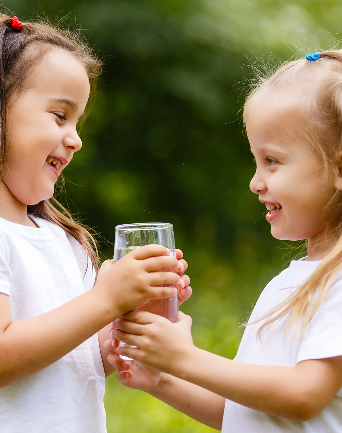 2 young girls outdoors sharing a glass of water