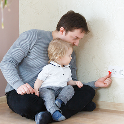 man inserting plug protector into wall with child on lap