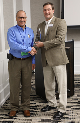 Two Men Standing Next to Each Other Shaking Hands, One Receiving Award