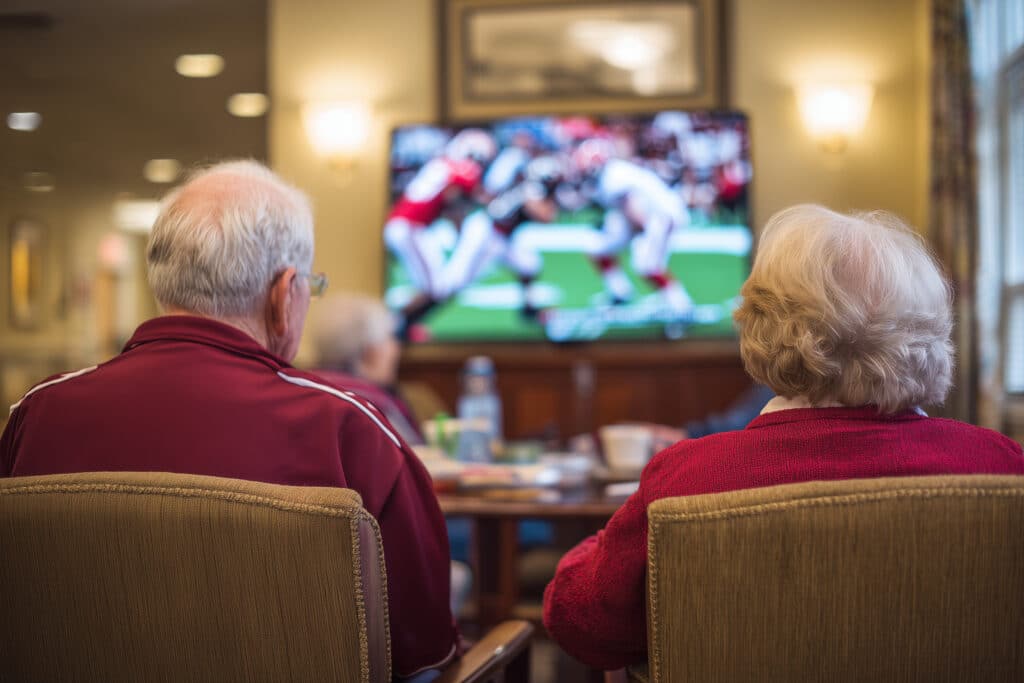 Image of two people watching TV. Location could be an assisting living facility. 