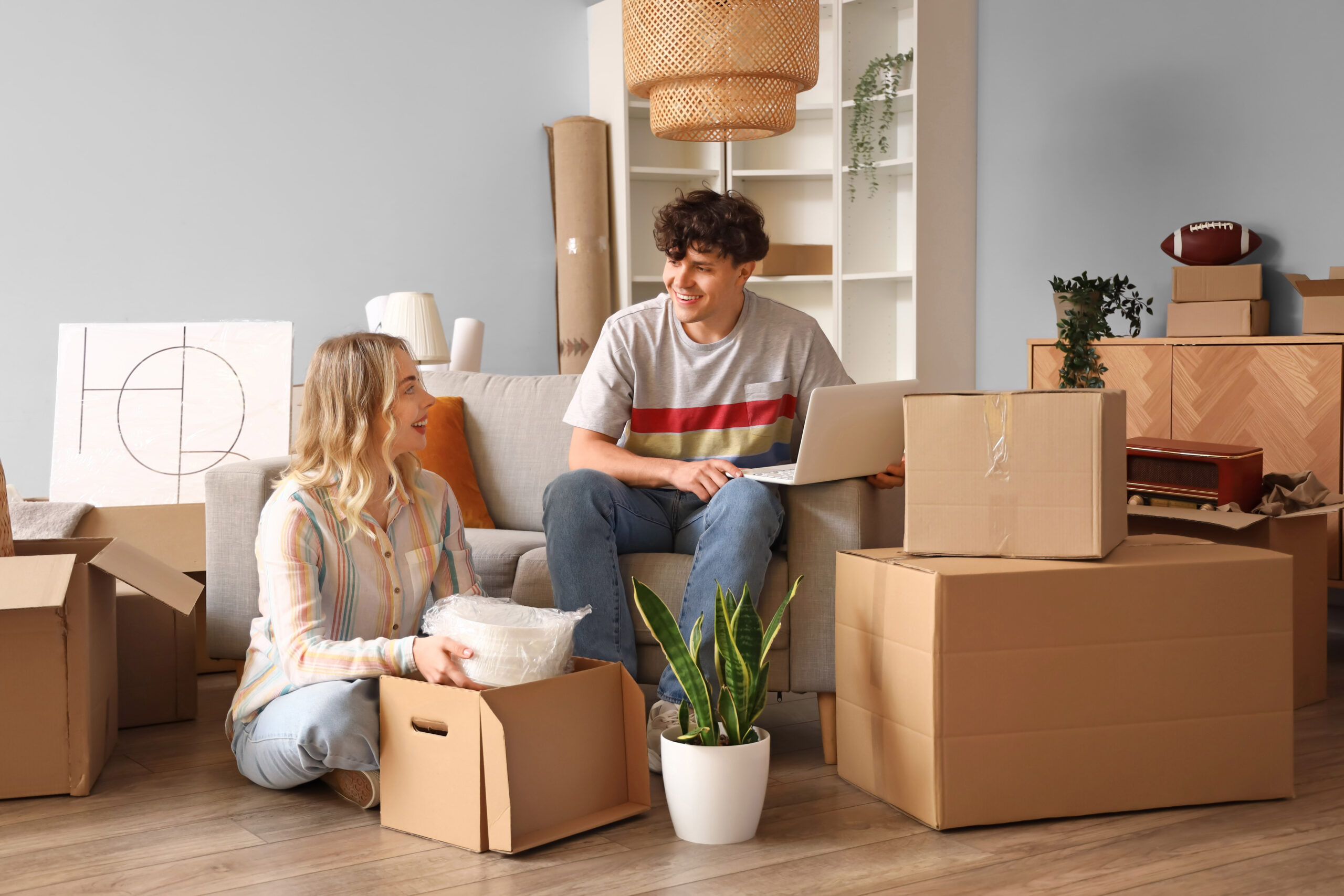 Young couple using laptop in room on moving day man and woman unpacking boxes in home