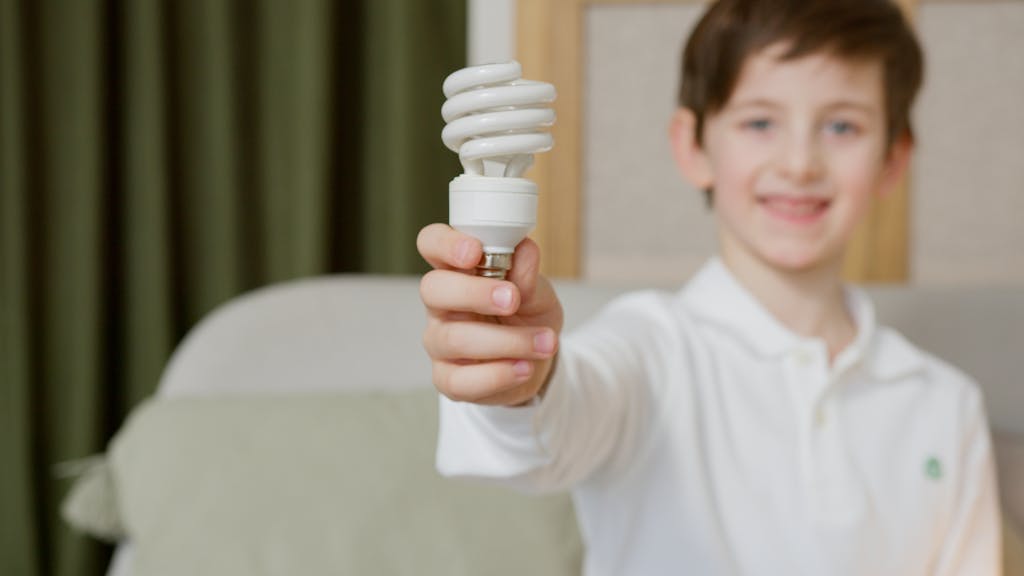 Young boy with light bulb promoting energy efficiency indoors.